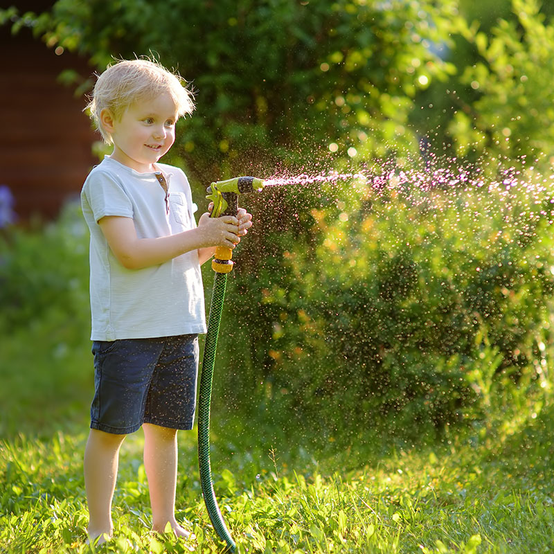 Einfache Gartenbewässerung mit der intelligenten Druckerhöhungsanlage Kind mit Gartenschlauch beim der Bewässerung